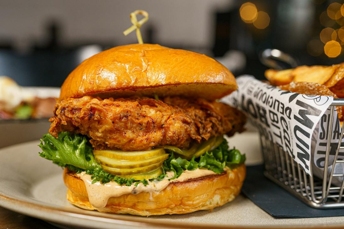 A fried chicken sandwich with pickles and lettuce next to a basket of fries