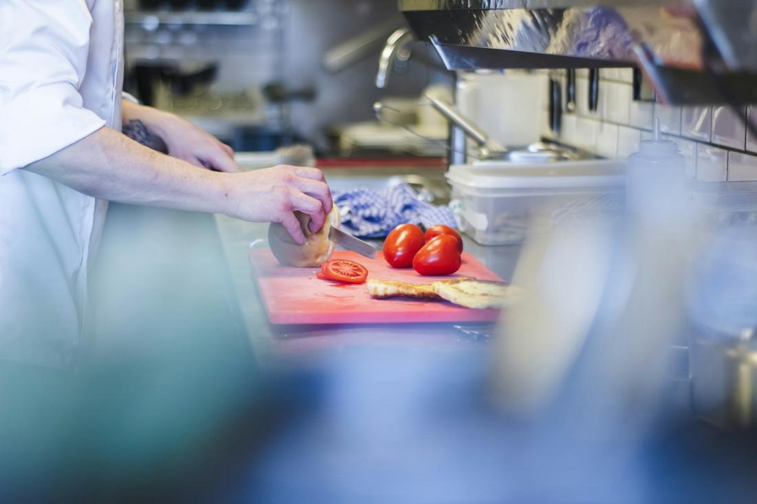 A cook slicing tomatoes on a red cutting board